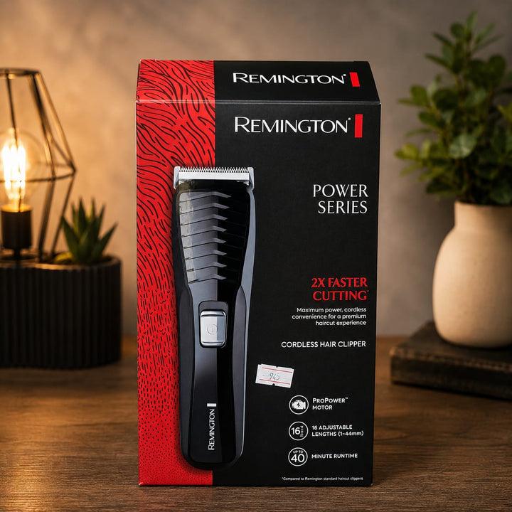 Caja de máquina cortadora de cabello inalámbrica Remington Power Series HC7130 en color negro y rojo. El empaque muestra la cortadora al frente e indica motor ProPower, 16 longitudes ajustables de 1 a 44 mm y hasta 40 minutos de autonomía. La caja está colocada sobre una mesa de madera con decoración de lámpara y plantas al fondo.